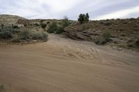 a desert road through the hills with some rocks and bushes on either side of the path