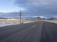 a lone deserted road leading into the desert under cloudy skies on a cloudy day with telephone poles