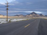 a lone deserted road leading into the desert under cloudy skies on a cloudy day with telephone poles