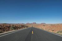 a desert road that leads out to the mountains in distance with a truck going under it