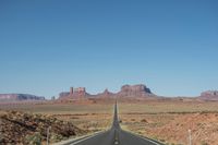 a desert road that leads out to the mountains in distance with a truck going under it