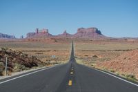 a desert road that leads out to the mountains in distance with a truck going under it