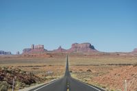a desert road that leads out to the mountains in distance with a truck going under it