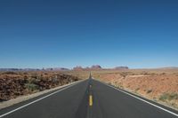 a desert road that leads out to the mountains in distance with a truck going under it