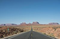 a desert road that leads out to the mountains in distance with a truck going under it