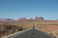 a desert road that leads out to the mountains in distance with a truck going under it