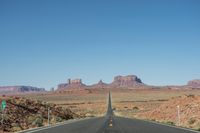 a desert road that leads out to the mountains in distance with a truck going under it