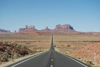 a desert road that leads out to the mountains in distance with a truck going under it