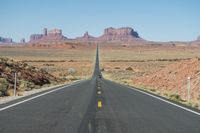 a desert road that leads out to the mountains in distance with a truck going under it
