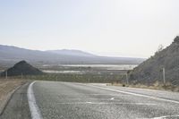 a motorcycle riding down a winding highway between hills and dry grass on a sunny day