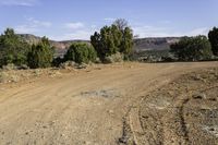 a dirt road with sparse brush on both sides and mountains behind it in the background