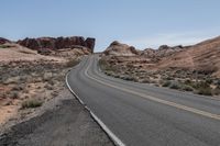 an empty desert road with mountains in the backgrund and rocks on both sides