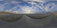 a 360 - lens panoramic view of a desert road under the cloudy sky