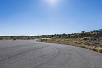 an empty empty road in the sun, with mountains in the distance behind it and a hill in the background