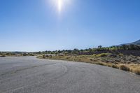 an empty empty road in the sun, with mountains in the distance behind it and a hill in the background
