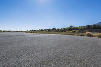 an empty empty road in the sun, with mountains in the distance behind it and a hill in the background