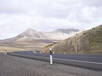 two parking meters stand in front of a desert road next to a hill filled with rolling hills