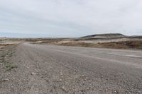 a dirt road is lined with dirt and weeds on either side of it in the distance is a plain