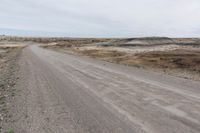 a dirt road is lined with dirt and weeds on either side of it in the distance is a plain