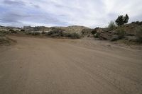 a small dirt road that leads through some dry brush and brush bushes, with hills in the background