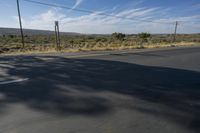 a motorcycle travels on an empty roadway in the desert countryside and has power lines, telephone poles and telephone lines