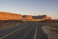 a paved road winding through the desert on a clear day with sunsets in the background