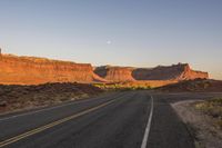 a paved road winding through the desert on a clear day with sunsets in the background