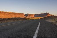 a paved road winding through the desert on a clear day with sunsets in the background