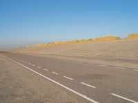 a long desert road that is lined with dirt and sand, with two trucks in the distance