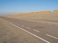 a long desert road that is lined with dirt and sand, with two trucks in the distance