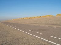 a long desert road that is lined with dirt and sand, with two trucks in the distance