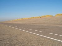 a long desert road that is lined with dirt and sand, with two trucks in the distance