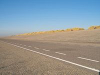 a long desert road that is lined with dirt and sand, with two trucks in the distance