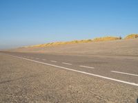 a long desert road that is lined with dirt and sand, with two trucks in the distance