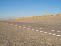 a long desert road that is lined with dirt and sand, with two trucks in the distance