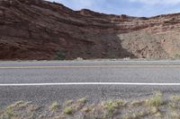 a person riding a motorcycle along a narrow road through rocks and sand cliffs a grassy area on both sides