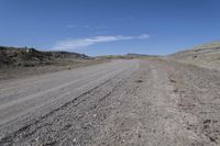 a dirt road is surrounded by some hills and desert like terrain as the vehicle sits on it