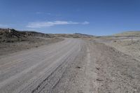 a dirt road is surrounded by some hills and desert like terrain as the vehicle sits on it