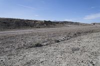 a dirt road is surrounded by some hills and desert like terrain as the vehicle sits on it