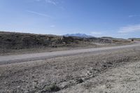 a dirt road is surrounded by some hills and desert like terrain as the vehicle sits on it