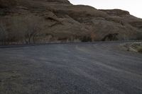 an empty desert road next to the edge of the mountains and valley, in the distance, the sun is set and the moon shines up over the hillsides