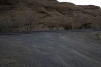 an empty desert road next to the edge of the mountains and valley, in the distance, the sun is set and the moon shines up over the hillsides