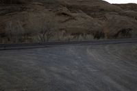 an empty desert road next to the edge of the mountains and valley, in the distance, the sun is set and the moon shines up over the hillsides