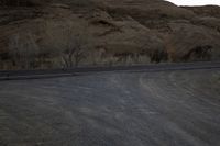 an empty desert road next to the edge of the mountains and valley, in the distance, the sun is set and the moon shines up over the hillsides