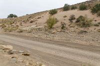 a dirt road through the desert with rocks and grass on it's sides and hills in the background