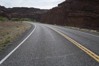 a person riding a motorcycle along a narrow road through rocks and sand cliffs a grassy area on both sides