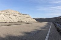 a paved road next to the mountains in a valley with dry grass and rocks on both sides