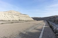 a paved road next to the mountains in a valley with dry grass and rocks on both sides