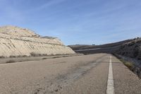 a paved road next to the mountains in a valley with dry grass and rocks on both sides