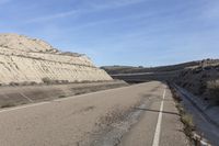 a paved road next to the mountains in a valley with dry grass and rocks on both sides